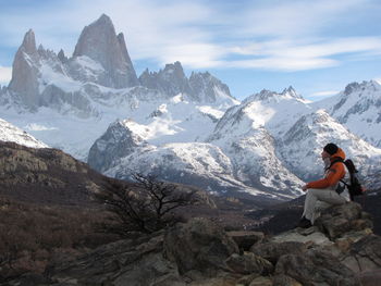 Man sitting on rock against snowcapped mountains