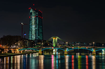 Illuminated bridge over river against buildings at night