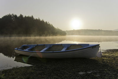 Boat moored on lakeshore with mist and bright newly risen sun