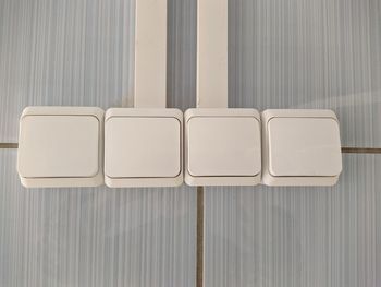 Four white light switches on a tiled wall