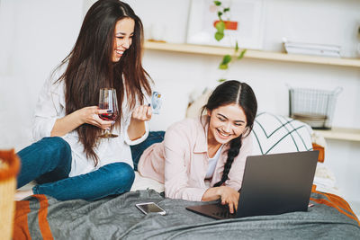 Woman shopping online through laptop while friend having wine at home