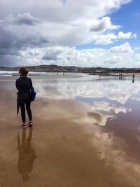 Rear view of woman standing on beach against sky