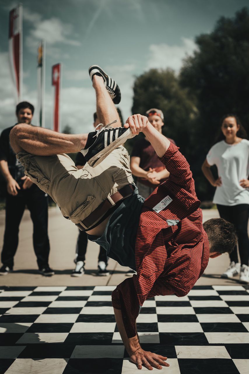 real people, full length, leisure activity, lifestyles, outdoors, dancing, day, performance, medium group of people, men, skill, sky, tree, young adult, breakdancing, finish line, people