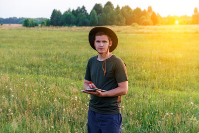 Young man farmer in cowboy hat at agricultural field on sunset holding tablet. happy man on nature 