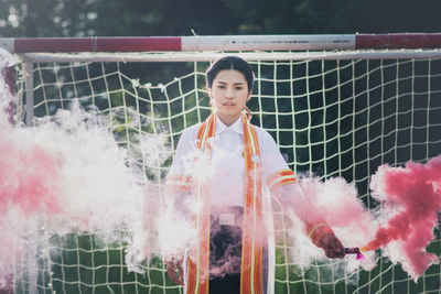 Portrait of woman holding distress flare while standing on soccer field
