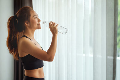 Side view of woman drinking water at home