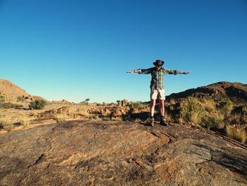 Man standing on rock against clear blue sky