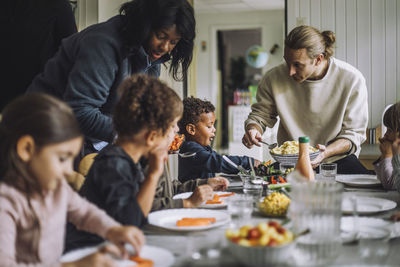 Male and female teacher serving food to children while having meal at table in kindergarten