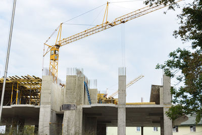 Low angle view of crane by building against sky