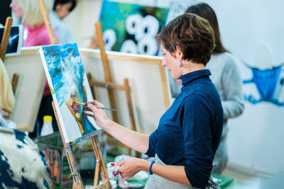 Side view of woman painting on canvas in studio