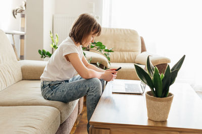 Distance learning. the girl is sitting on the couch with a phone in her hands