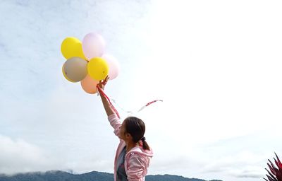 Rear view of woman with balloons against sky