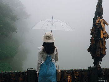 Rear view of woman with umbrella standing against sky