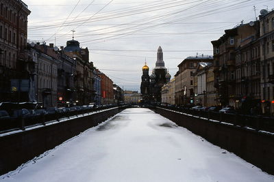 Snow covered road amidst buildings in city against sky