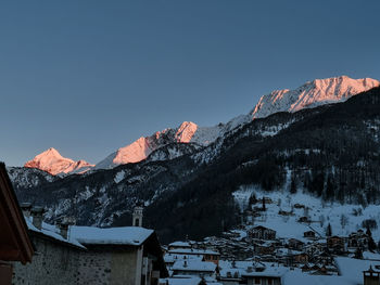 Houses by snowcapped mountains against clear sky during winter