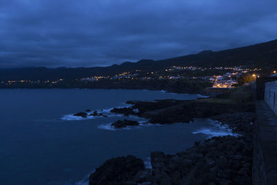 Illuminated buildings by sea against sky at night