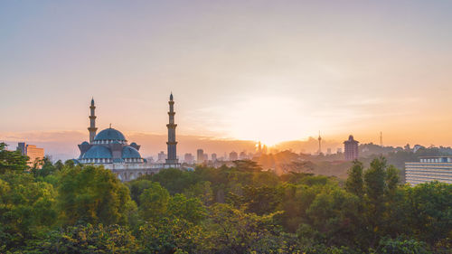Federal territory mosque by trees against sky during sunset