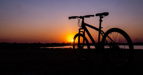 Silhouette bicycle on field against sky during sunset