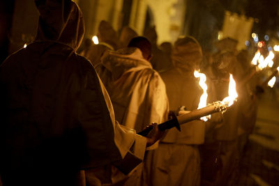 Rear view of people with flaming torch walking on street at night