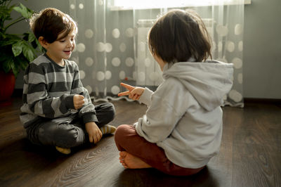 Brothers playing rock paper scissors on floor at home