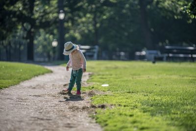 Full length of boy standing amidst grassy field on walkway during sunny day