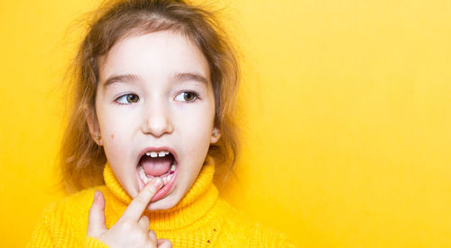 Close-up of girl touching teeth against colored background