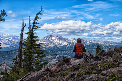 Rear view of man standing on mountain against cloudy sky