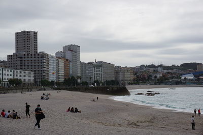 People on beach by buildings against sky