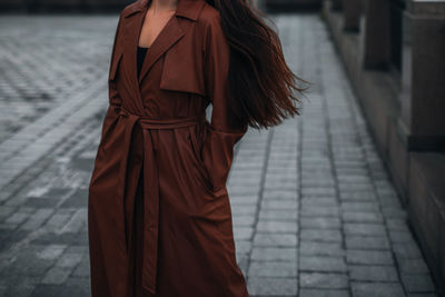 Woman walking alone in the city. fancy details of autumn long brown leather trench coat. street styl