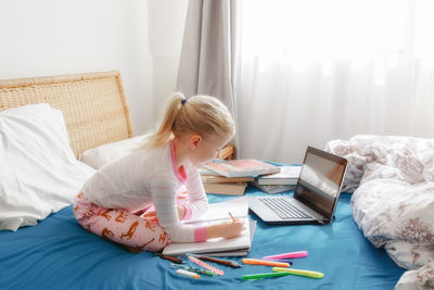 Side view of girl studying with laptop on bed at home