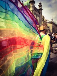 Rear view of man walking on street in multi colored costume by historic building at pay pride