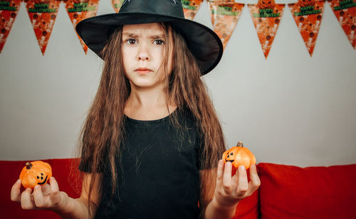 Girl in a halloween hat with pumpkins in her hands.