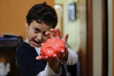 Close-up portrait of boy holding red clay at home 