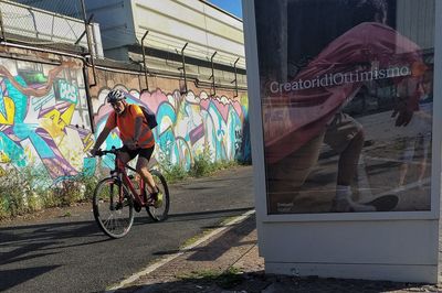 Man riding bicycle with graffiti on wall in city