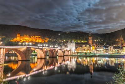 Illuminated bridge over river in city against sky