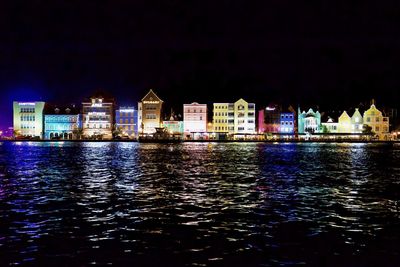 River by illuminated buildings against sky at night