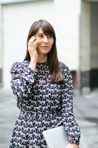 Portrait of a professional woman using phone and holding laptop standing outdoors