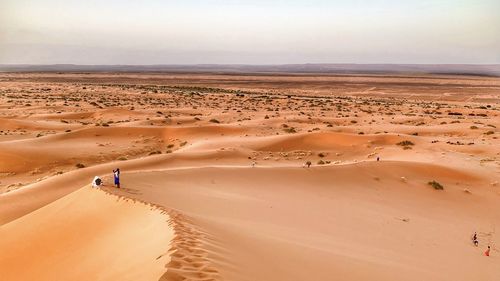 Scenic view of desert with woman standing on sand against sky