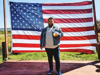 Portrait of man having drink while standing against american flag