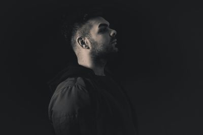 Portrait of young man looking away against black background