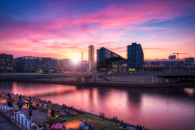 River by buildings against cloudy sky during sunset