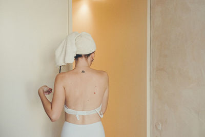 Midsection of shirtless young woman standing against wall at home