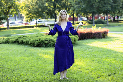 Beautiful blonde in purple dress is balancing in public park and holding a small balls