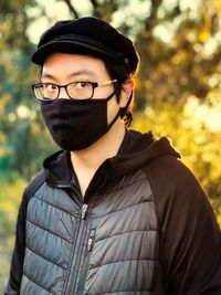 Portrait of young man with eyeglasses standing against trees