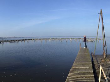 Side view of man standing on pier over lake against sky