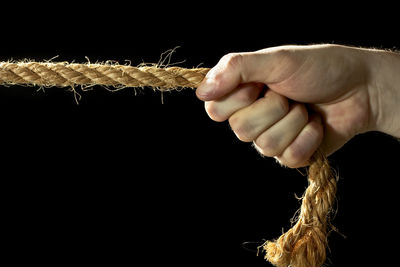 Close-up of hand holding rope over black background