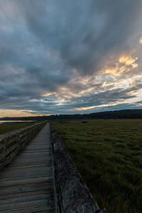 Empty road amidst field against sky during sunset