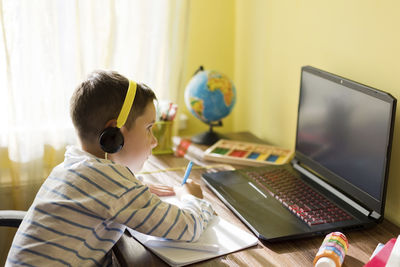 Boy wearing headphones using laptop at home