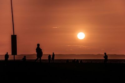 Silhouette people at beach against sky during sunset