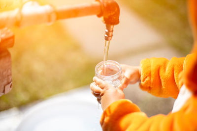 Faceless child fill the glass with water in water tap outdoor person